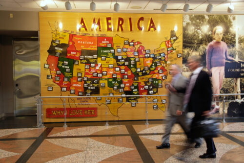 Colorful map of the United States highlighting different states, labeled "AMERICA" at the top, with people walking in front.